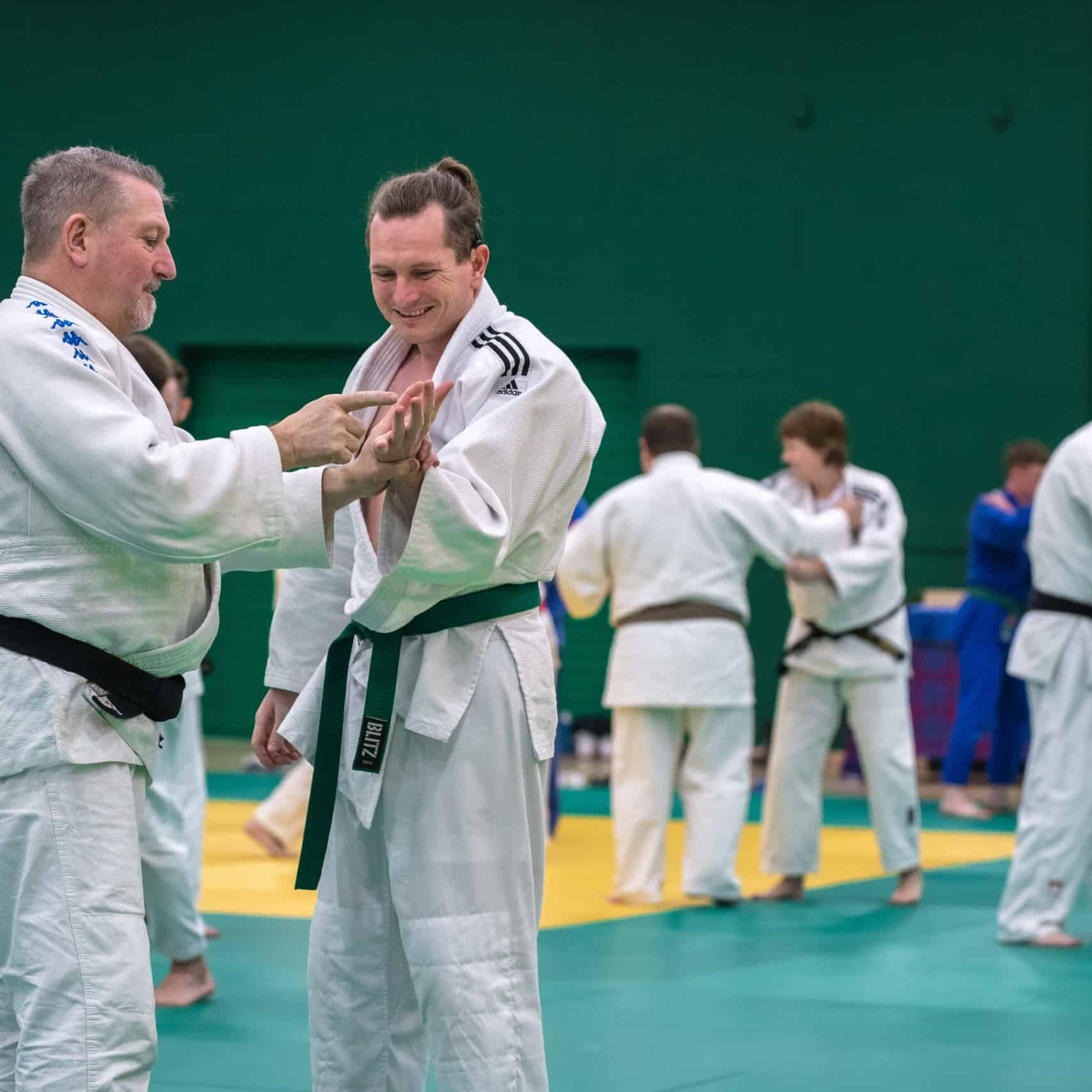 Judoka Chris Nicol with club coach Charlie Strachan communicating through tactile sign language on a judo mat.