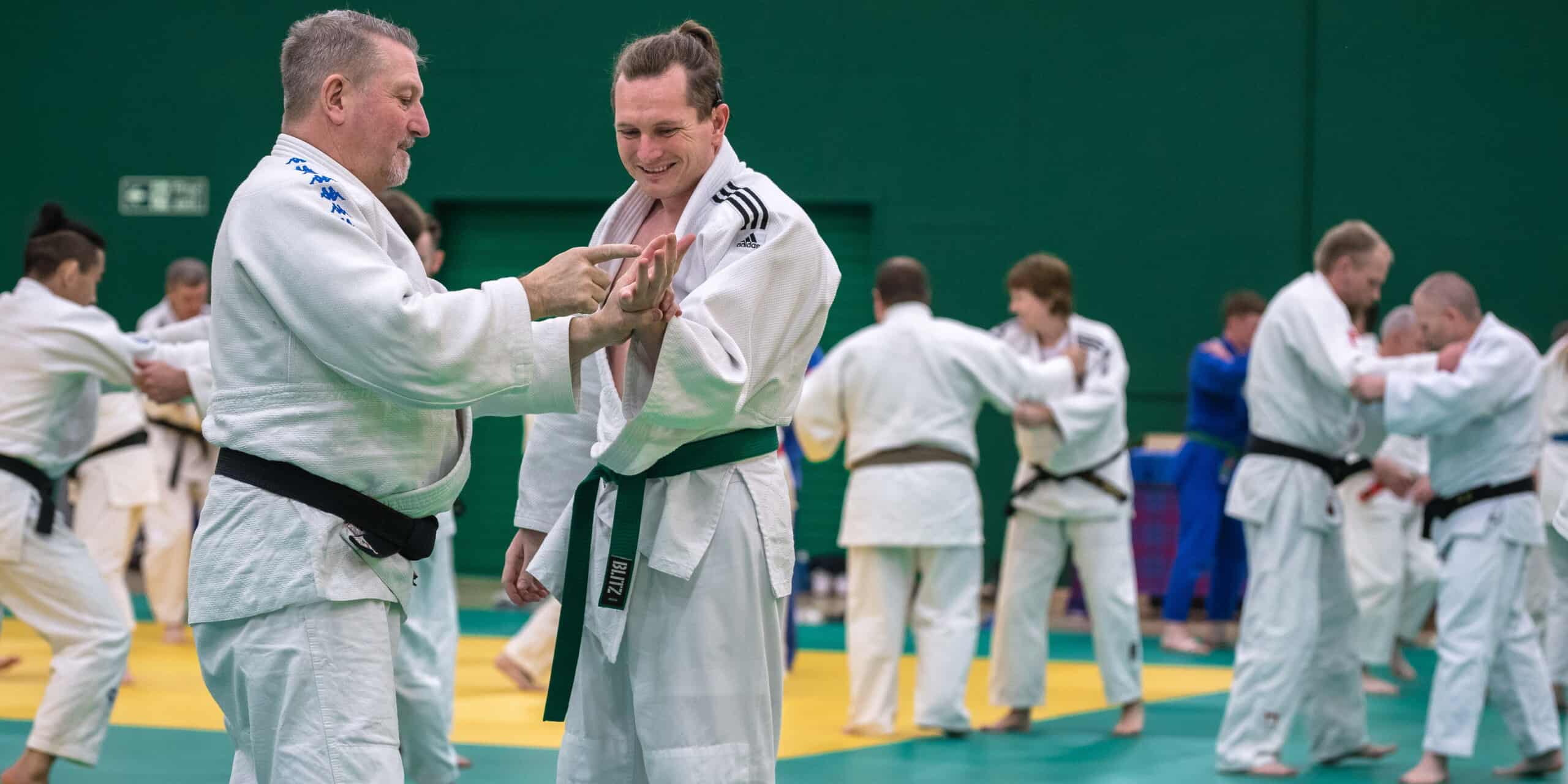 Judoka Chris Nicol with club coach Charlie Strachan communicating through tactile sign language on a judo mat.